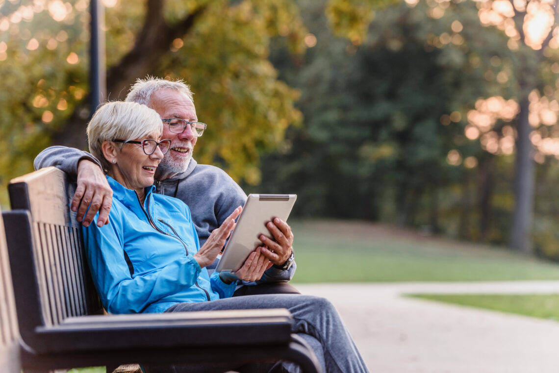 Study recruitment photo depicting and older couple on a park bench looking at an electronic tablet together