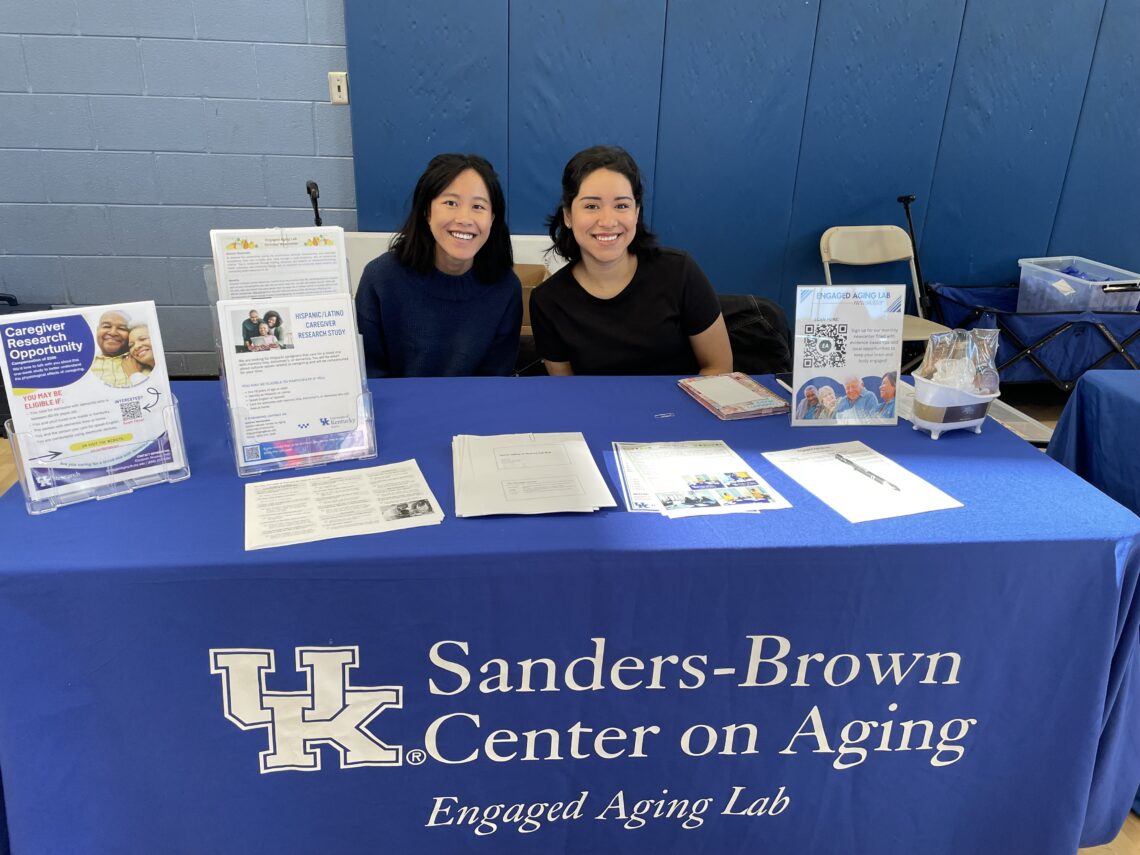 Nancy and Andrea sit behind Engaged Aging Lab table at the YMCA Senior Health Fair